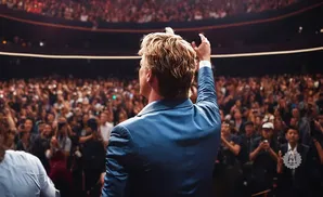 A man in a blue suit raises his arm to a cheering audience.