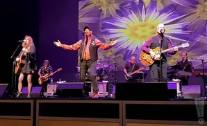 A band performs on stage with a large floral projection behind them.