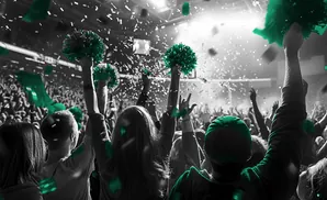A crowd cheers with green pom-poms and confetti during a concert or sporting event.