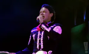 A man in a black and pink mariachi outfit sings into a microphone onstage.