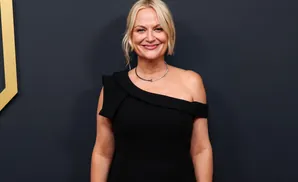 A blonde woman in a black off-the-shoulder dress smiles warmly at the camera.