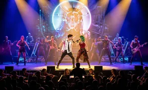 A band performs on stage with an orchestra in the foreground.