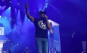 Rapper T.I. performs on stage in front of a large screen and blue lights.