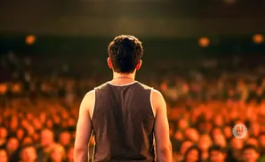 A man in a tank top stands with his back to the camera, facing a blurred, cheering crowd.