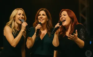 Three women singing into microphones on stage.