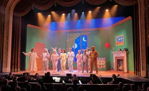 Performers in pajamas and animal costumes on stage with an orchestra in the foreground.