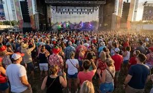 Large crowd of people at an outdoor concert, facing a stage with performers.