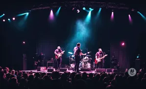 A band performs on a dimly lit stage with purple and blue spotlights.