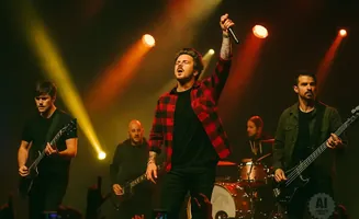 A band performs on stage with a singer in a red plaid shirt holding a microphone up.