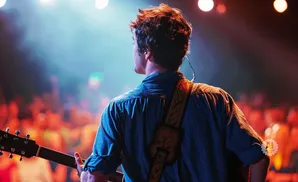 A man plays guitar on stage with a blurred audience in the background.