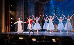 Ballet dancers in a snowy scene, with ballerinas in light blue tutus and a boy in a red jacket and white pants.