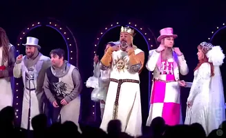 A group of performers in knight and princess costumes on stage with a bright archway behind them.
