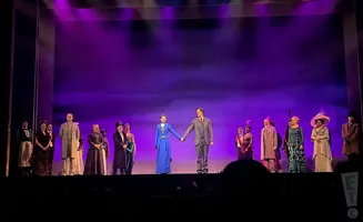 A theater cast bows on stage in front of a purple backdrop.