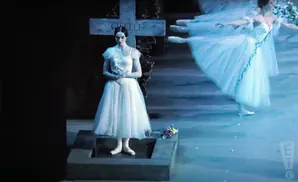 Ballerinas in white tutus dance on stage. One stands in the foreground before a gravestone marked 