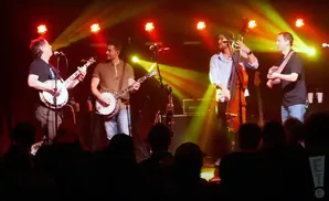 A band plays on a dimly lit stage, illuminated by yellow and red spotlights.