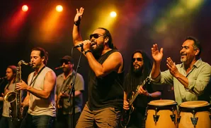 A band performs on stage with a singer, saxophonist, guitarist, and conga players under colorful stage lights.