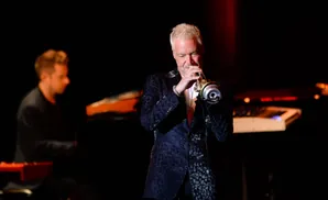 A man plays a trumpet on stage, wearing a dark jacket with a leopard-like pattern.