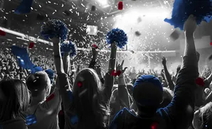 Crowd cheering with blue and red confetti and pom-poms, mostly in grayscale.