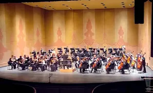 An orchestra performs on stage in front of a large, painted backdrop.