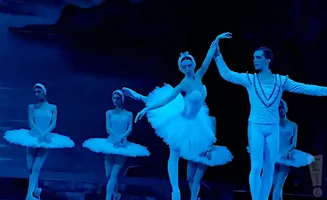 Ballerinas in white tutus and a male dancer in a light blue costume on a dark stage.