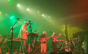 A band performs on stage with green and orange lighting.