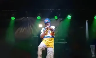 Rapper performing on stage, wearing a blue baseball cap and colorful jersey, holding a microphone.