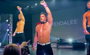 Chippendales dancers in black pants and pink accessories perform on stage.