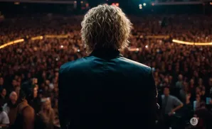 A person with curly blonde hair stands facing a large, blurred crowd in an arena.