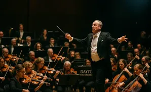 Conductor leads an orchestra during a performance, with musicians playing violins and cellos.
