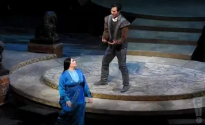 Opera singers in costume on a circular stage with blue and gray designs.