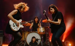 Three women performing on stage with guitars and drums.