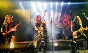 Three guitarists perform on stage with dramatic lighting.
