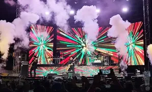 Band performing on a stage with a colorful, abstract light show backdrop and smoke effects.
