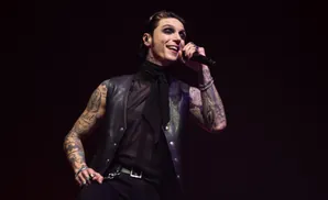 A tattooed man with heavy eye makeup sings into a microphone.