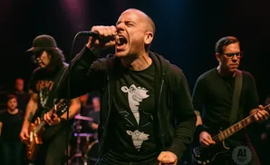 A bald man screams into a microphone on stage with his band.