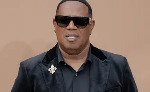 Master P wears sunglasses and a black velvet blazer with a fleur-de-lis brooch.