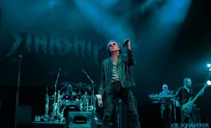 Mickey Thomas of Starship performs on stage in a leather jacket.