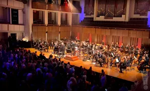 An orchestra performs for a live audience in a concert hall.