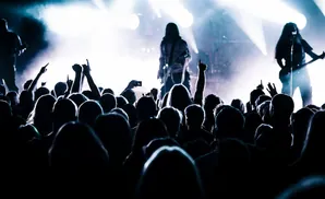 A crowd silhouetted against bright stage lights at a concert, with some people raising their hands.