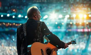 Man with guitar on stage, crowd in the background.