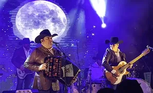 A mariachi band performs on stage under a giant moon projection.