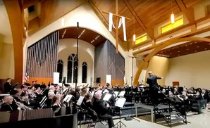 An orchestra in a church, with a conductor leading them and an organ in the background.
