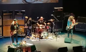 A band performs on stage with large amplifier stacks and a drummer.