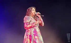 A woman in a colorful dress sings into a microphone on stage.