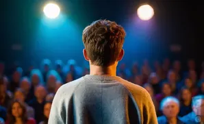 Back of a man's head facing a blurred audience, illuminated by stage lights.