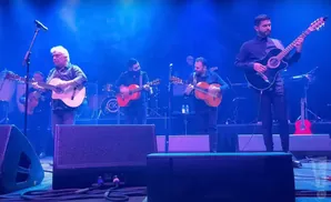 A band plays guitars on a brightly lit stage.