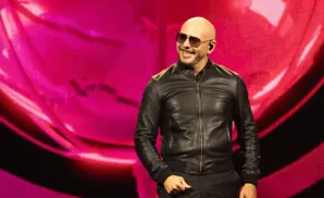 Pitbull wearing sunglasses and a black leather jacket smiles on a pink stage background.