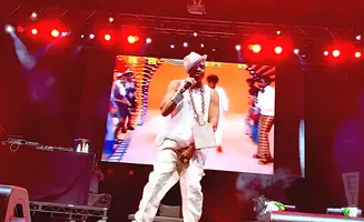 Rapper Flavor Flav performs on stage wearing white, a fedora, and a large gold chain.
