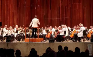 Orchestra in white jackets performs on stage with a conductor.