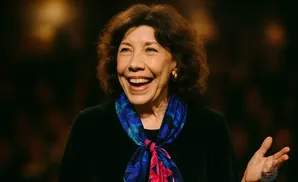 Lilly Tomlin laughs and gestures with her hand, wearing a black shirt and a floral scarf.